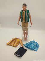 Full view of doll standing in glass, extra clothing laid out