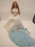 Full view of Barbie doll in white wedding dress with blue gown laid in front