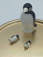 Front view of plastic penguin salt shaker beside two penguin brooch pins