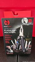 Front of sealed retail box showing Smart Gear USB rechargeable flashlight multitool and 12 functions icon