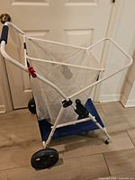 Full view of white framed folding beach cart with mesh basket and blue base