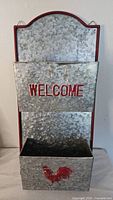 Front view showing two galvanized pockets, red trim, 'WELCOME' text and rooster graphic