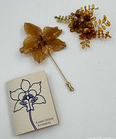 Front view of orchid stick pin, resin brooch, and original card