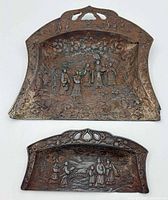 Front view of both ornate metal trays showing embossed scenes