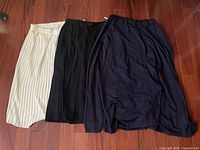 Three skirts side by side: ivory pleated, black pleated, navy layered