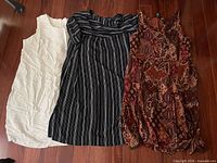 All three garments laid flat: cream tunic, striped tunic, paisley dress