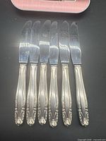 Six sterling silver-handled dinner knives laid out blade upward