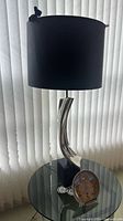 Full view of lamp on glass table showing chrome base and black shade