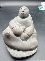 Front view of soapstone Inuit figure seated with arms on knees showing carved motif