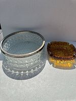 Both items side by side: clear cut glass bowl with metal rim and amber bubble ashtray