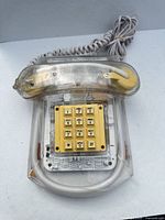 Front view of clear plastic telephone showing yellow keypad and coiled handset cord