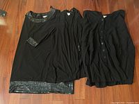 Three black garments laid out: sequin-trim tunic, open cardigan, button-front piece