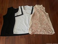 All three sleeveless tops laid flat: black embellished, white with black trim, cream with lace