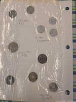 Overview of nine coins in binder sheet with handwritten denomination notes