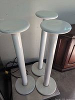 Three white metal stands grouped together showing overall form, tops and bases