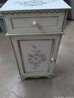 Front view showing floral design, drawer, cabinet door, knobs, scalloped base