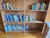 Two upper shelves of wooden bookcase filled with assorted hardcover and paperback books