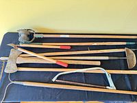 Overall view of six long-handled garden and forestry tools laid on table