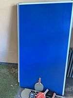 Folded blue table halves leaning against wall with paddles and hardware visible