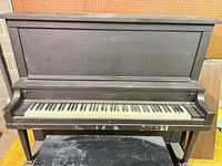 Front view of black Chickering Acoustigrande upright piano, full keyboard visible, bench partially visible