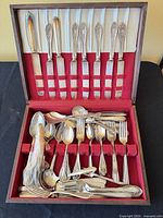 Flatware set displayed in open wooden chest showing knives, forks, spoons and serving pieces