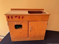 Front view of wooden play kitchen base cabinet showing countertop cut-out, red knobs, cabinet doors