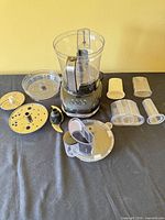 All components laid out including base, bowl, lid, blades, discs, pushers, cups