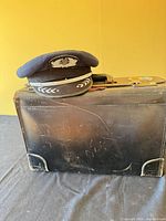 Cap resting atop scuffed black leather briefcase front view