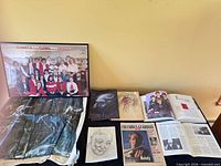 Overview of all items laid on table including framed photo, drawings, abstract poster, newspaper, Beatles pages