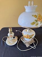 Both lamps side by side showing milk glass bodies, floral pattern, ornate bases, cords