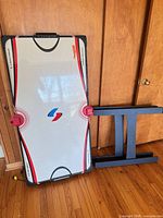 Air hockey tabletop with detached legs and two red mallets