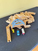 Pile of wooden track pieces, bridge parts, Thomas engine, red car, crossing sign visible