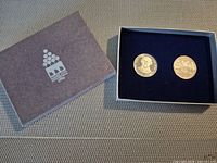 Presentation box and two coins displayed in felt insert