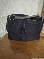 Front view of black suede shoulder bag showing tassel and shoulder strap with gold-tone ring