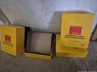 Three Kodak photographic paper boxes, one open showing interior, two closed with lids