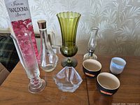 All eight items on table: bud vase, box, green vase, carafe, glass bowl, oil lamp, two Baileys cups, blue floral cup