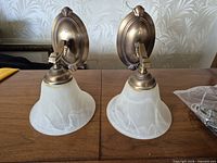 Pair of brass wall sconces with frosted shades upright on table
