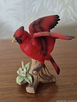 Front view of red porcelain cardinal on branch with flower