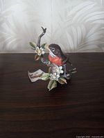 Front view of Lofton porcelain robin figurine on branch with blossoms and hang tag