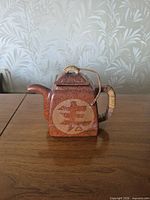 Front view of square ceramic teapot showing decal, handle, spout and lid