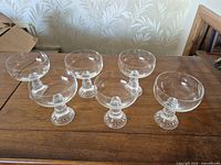 Full set of six pressed glass coupe glasses on wood surface