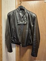 Front view of black leather biker jacket on hanger