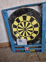 Front view of sealed dartboard set showing board, darts and instructions