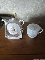 Teapot and cup set in retail sleeve alongside lidded mug on tabletop