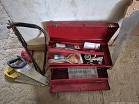 Overall view of toolbox with open lids, drawers closed, three saws leaning beside