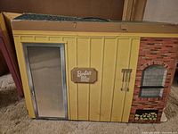 Yellow exterior wall panel showing door, brick barbeque and Barbie’s Dream House logo