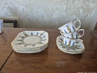 Stack of six square plates and stack of three cups on saucers showing pattern and shape