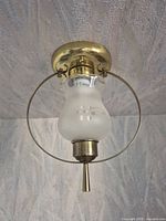 assembled fixture mounted to ceiling showing brass canopy, hoop, frosted shade, pull rod