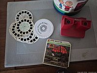 Red View-Master viewer, three reels, The Love Bug sleeve, Peanuts canister visible