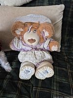 Front view of Hattie Furskin bear seated on sofa, showing dress and bonnet